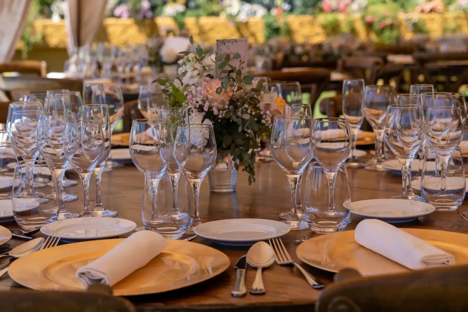 A long banquet table set with wine glasses, napkins, gold plates and a flower centrepiece