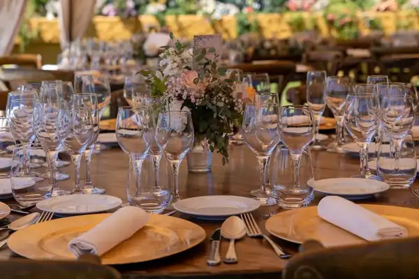 A long banquet table set with wine glasses, napkins, gold plates and a flower centrepiece