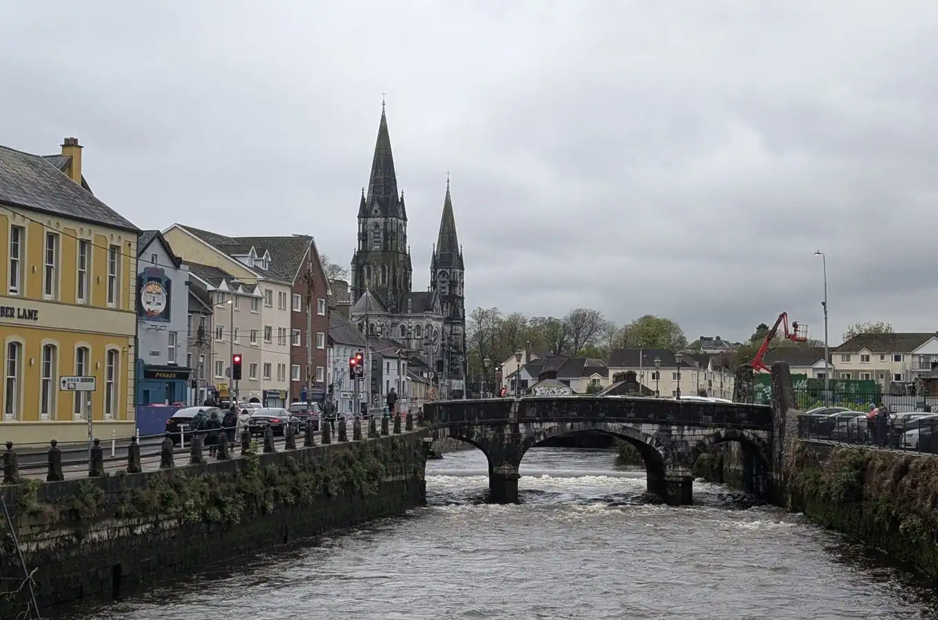 A stone bridge over an old-town river beneath colourful houses and church spires on a grey day